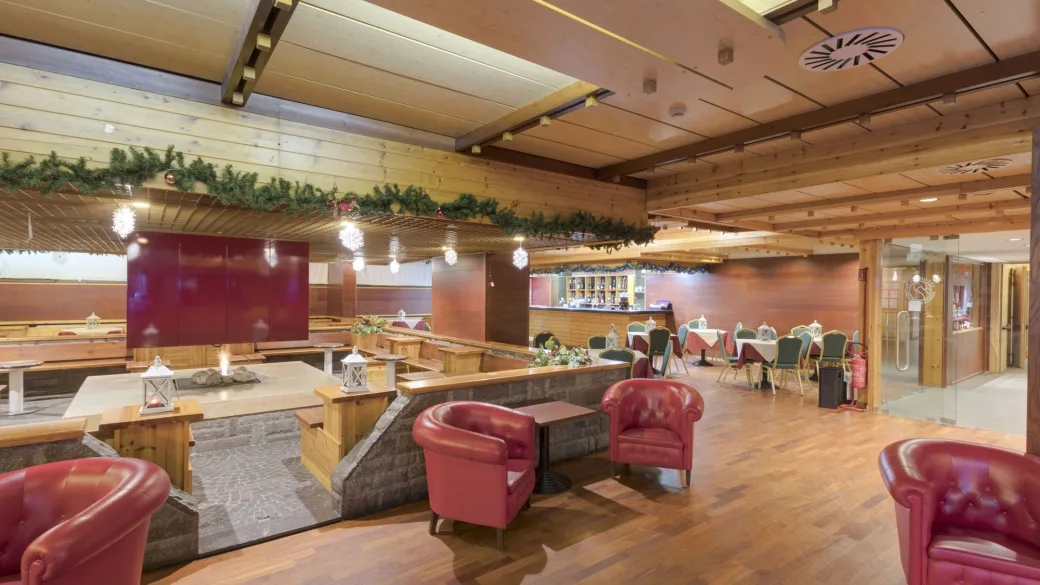 Ampia sala lounge in stile alpino con poltrone in pelle rossa, panche in legno e area bar