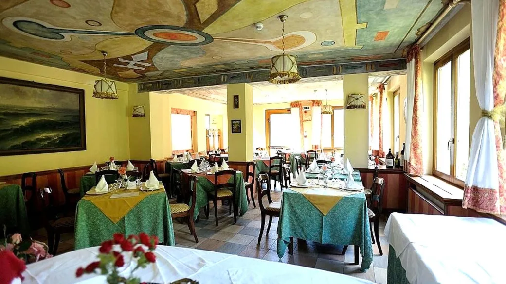 Sala ristorante interna con soffitto affrescato, tavoli apparecchiati con tovaglie verdi e gialle e lampadari in stile
