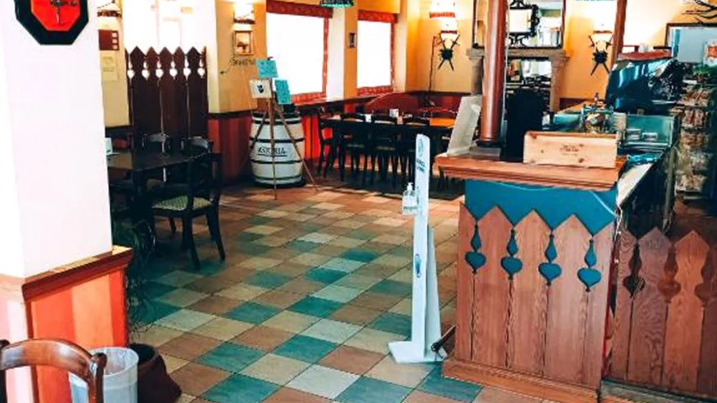 Interno dell'hotel con zona bar e ristorante, pavimento in piastrelle colorate, arredi in legno e dispenser di gel igienizzante