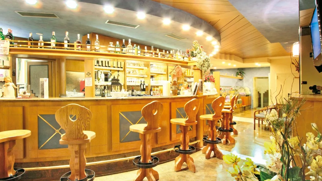 Bar dell'hotel con bancone in legno, sgabelli in legno intagliato e bottiglie esposte