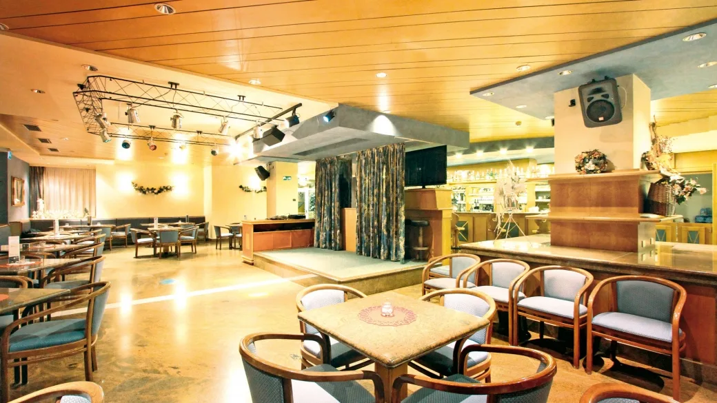 Sala lounge con divani, tavolini, bar e piccolo palco con impianto audio