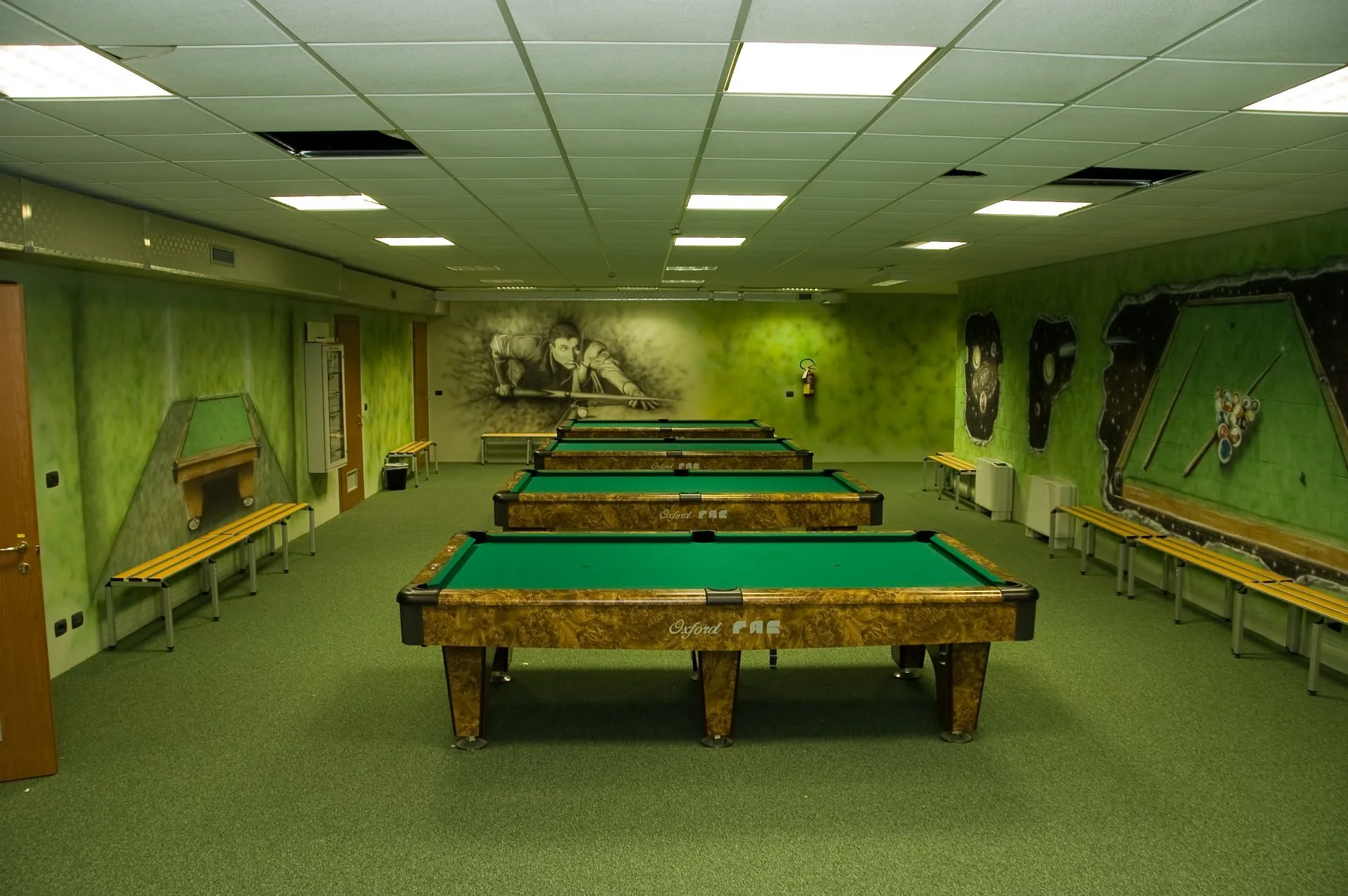 Sala biliardo con più tavoli verdi e murales a tema