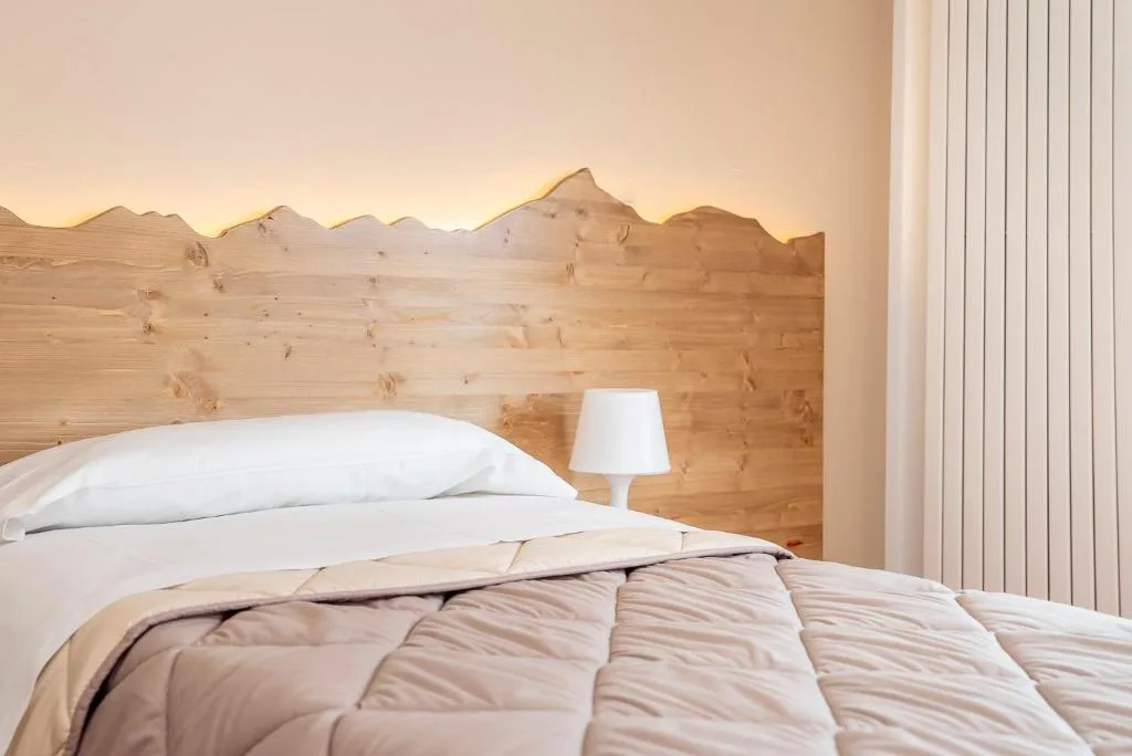 Camera con letto singolo e testiera in legno illuminata a profilo di montagne