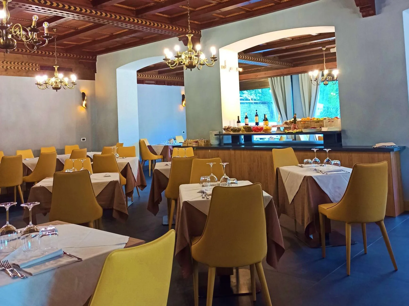 Sala ristorante con buffet, sedie gialle e soffitto in legno con lampadari