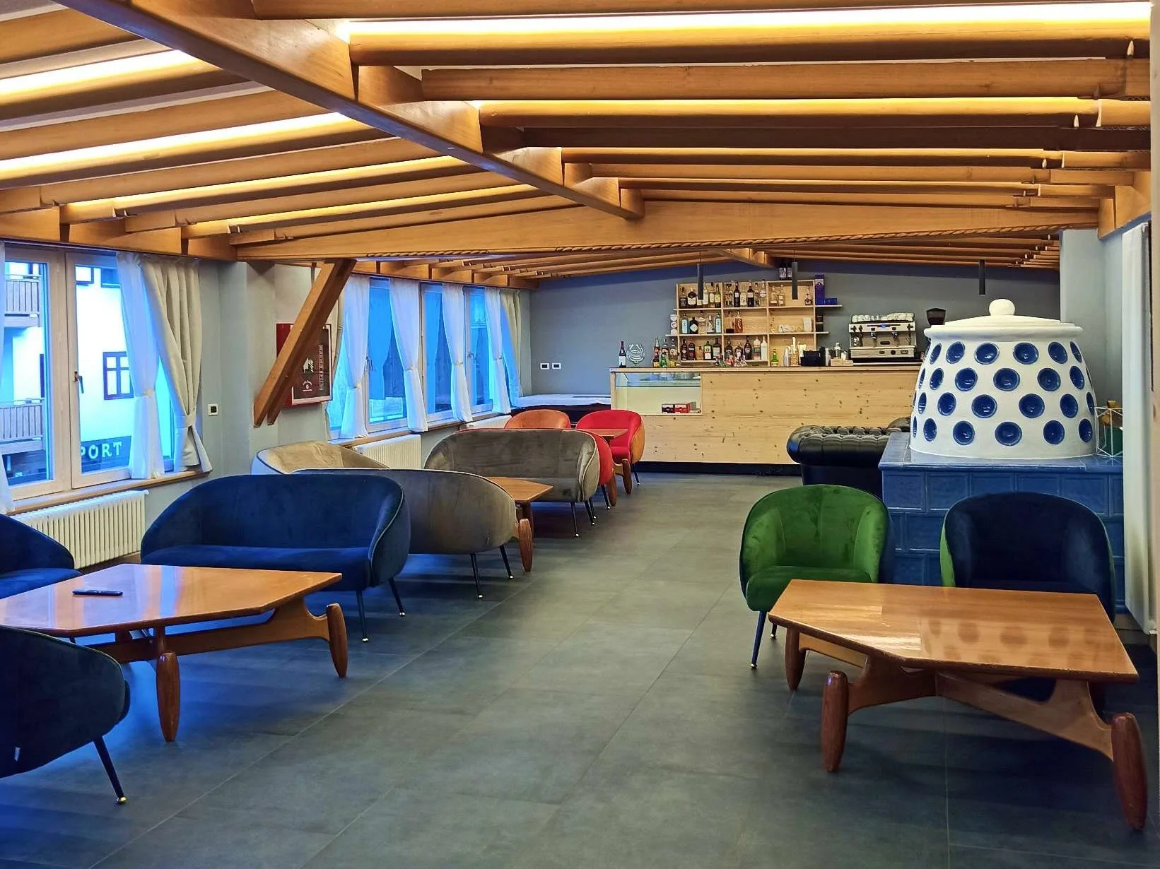 Area lounge bar con poltrone colorate, tavolini in legno e stufa in ceramica bianca e blu