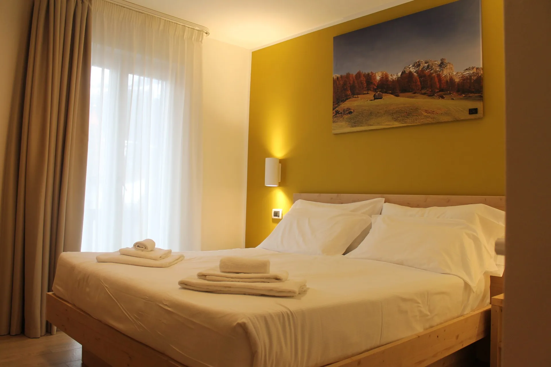 Camera matrimoniale con parete gialla, letto in legno e finestra con tende chiare