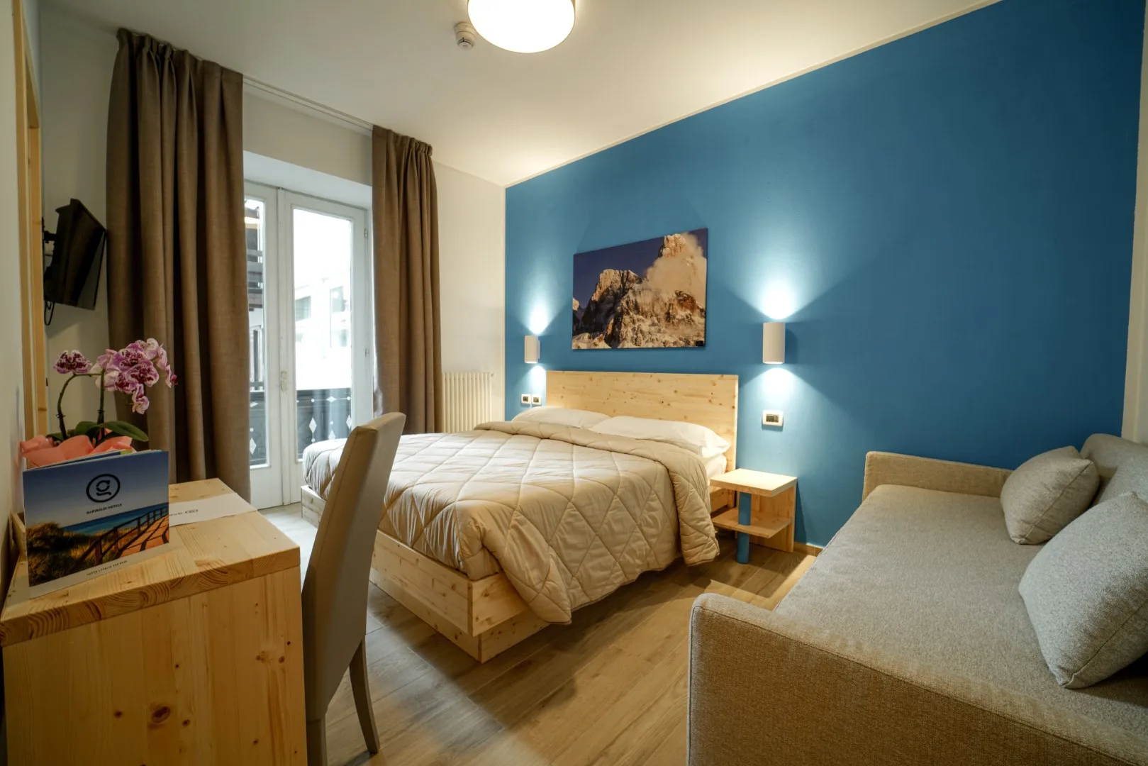 Camera matrimoniale con parete blu, letto in legno, divano e balcone