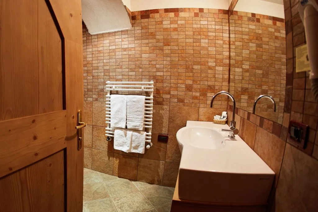Bagno con rivestimento a mosaico marrone, lavabo, scaldasalviette e porta in legno