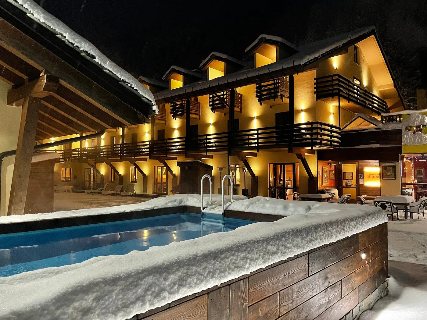 Piscina esterna coperta di neve con hotel illuminato di sera sullo sfondo in ambiente invernale