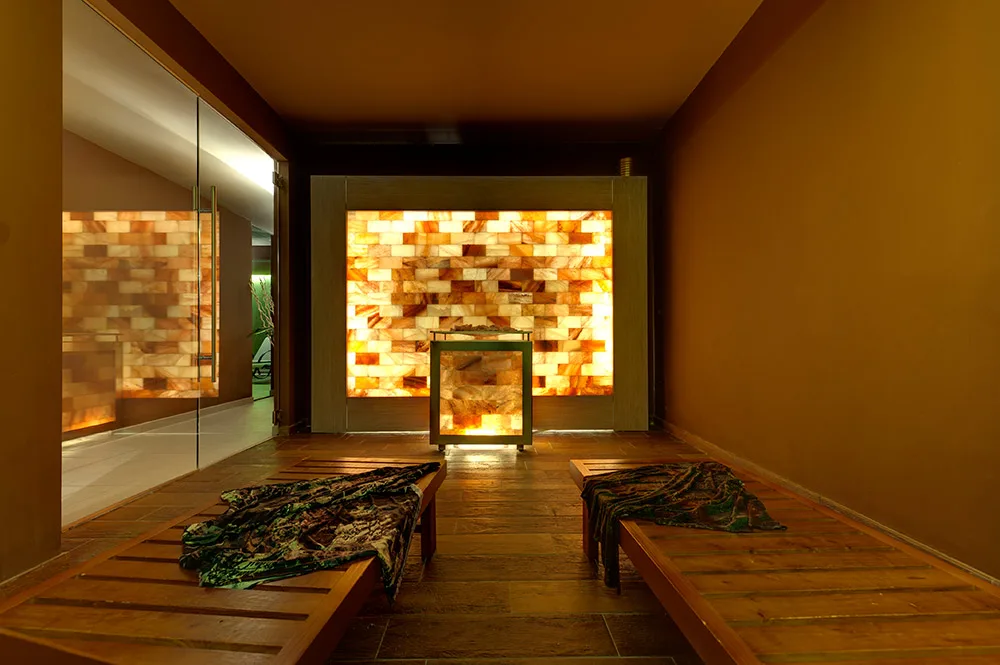 Sala della spa con parete illuminata in sale rosa e panche in legno con teli