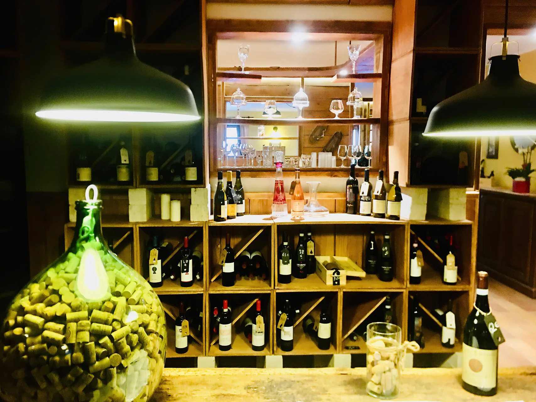 Angolo cantina con bottiglie di vino su scaffali in legno e damigiana con tappi di sughero
