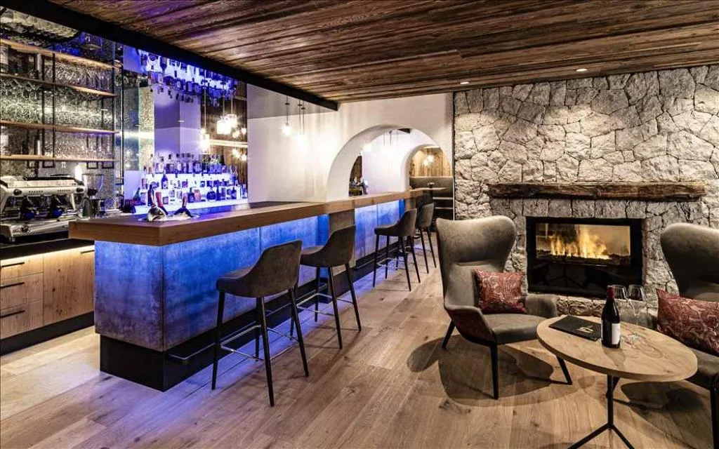 Bar lounge con bancone illuminato, camino a legna e poltrone accoglienti