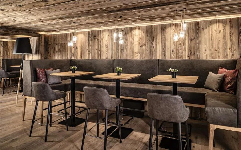 Zona lounge con tavoli alti, sgabelli e pareti rivestite in legno rustico