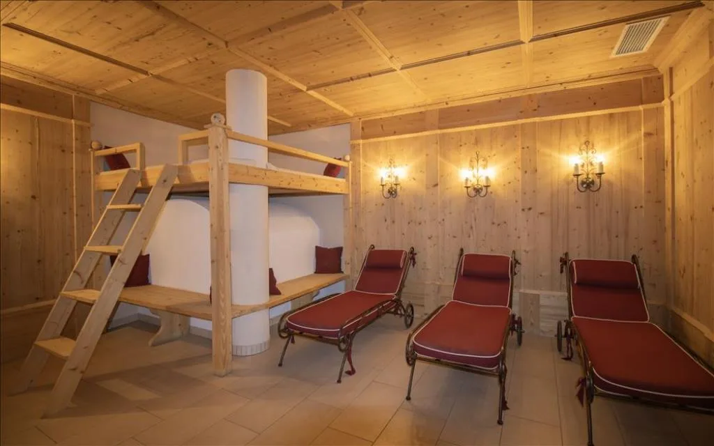 Sala relax con rivestimenti in legno, lettini imbottiti rossi e letto a soppalco