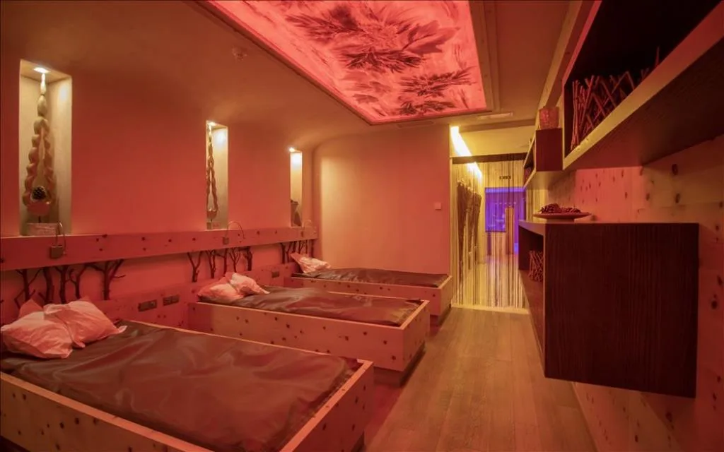 Sala relax della spa con lettini in legno di cirmolo e soffitto illuminato decorato