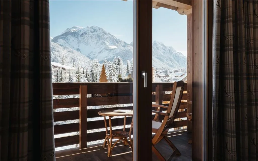 Vista dalla camera verso il balcone con tavolino e panorama montano innevato