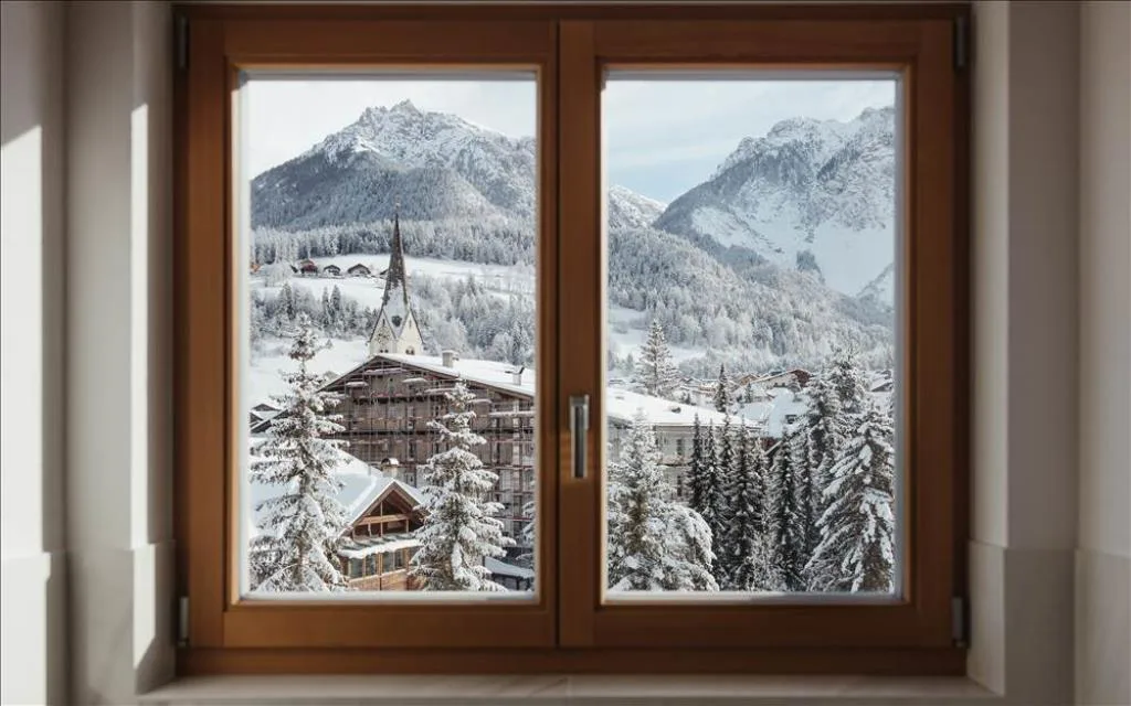 Finestra in legno con vista su paese e montagne innevate delle Dolomiti