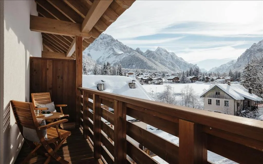 Balcone in legno con sedie e vista sulle case e montagne innevate