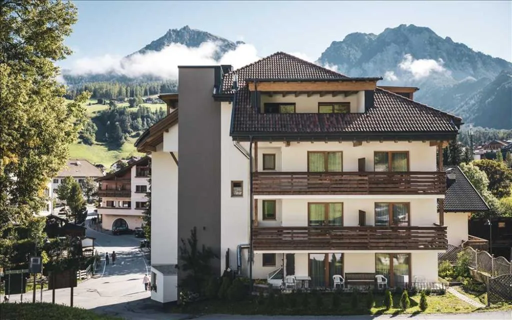 Facciata dell'hotel con balconi in legno e montagne sullo sfondo in estate