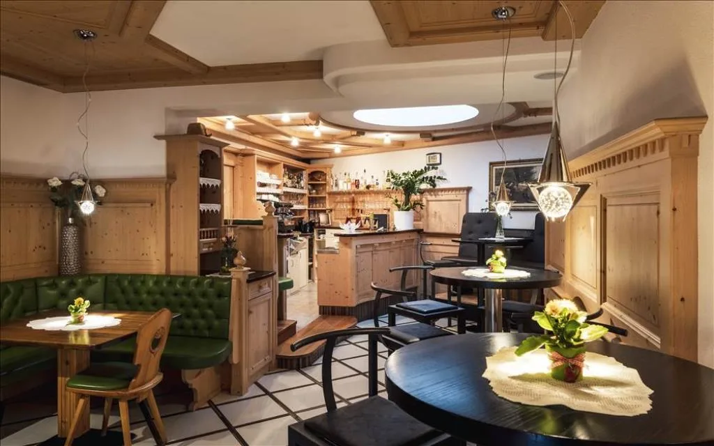Zona bar e soggiorno con boiserie in legno e divani in pelle verde