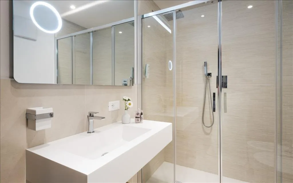 Bagno moderno con doccia in vetro, lavabo bianco e specchio illuminato