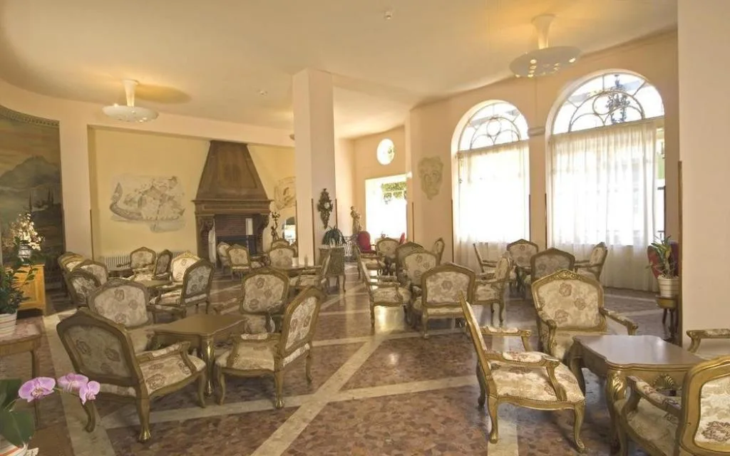 Salone interno in stile classico con poltrone eleganti, camino e ampie finestre ad arco