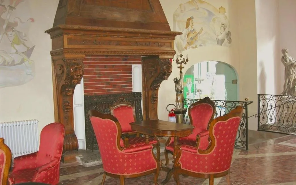 Salottino con camino in legno intagliato, poltrone rosse e affreschi alle pareti
