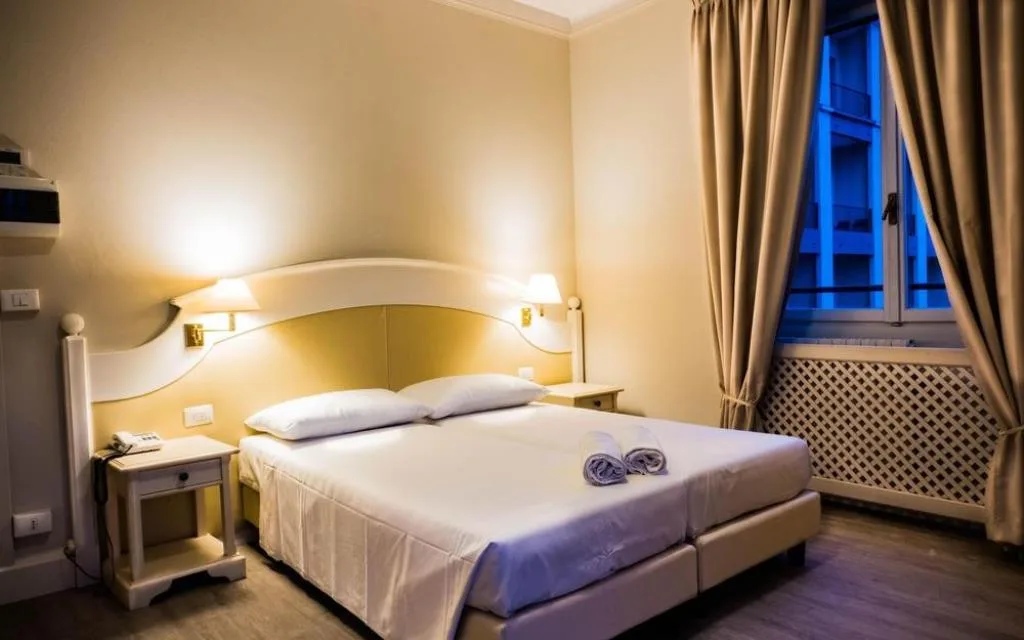 Camera classica con letto matrimoniale, testiera bianca e lampade da comodino
