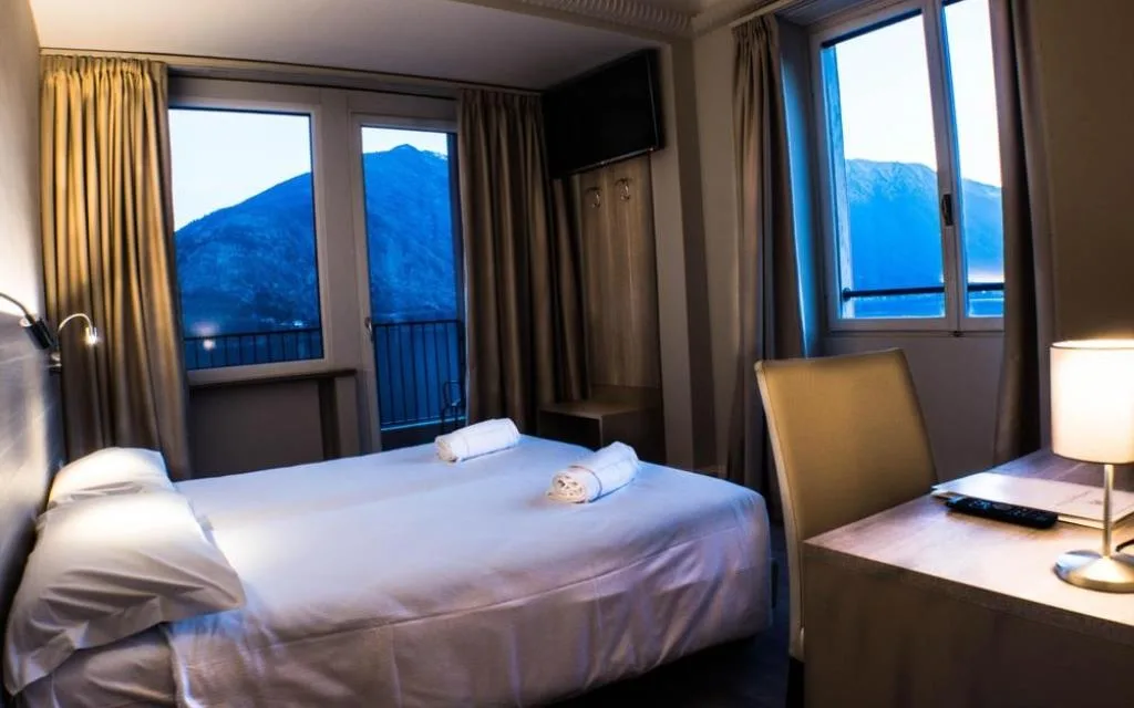 Camera d'albergo con letto matrimoniale e due grandi finestre con vista sulle montagne