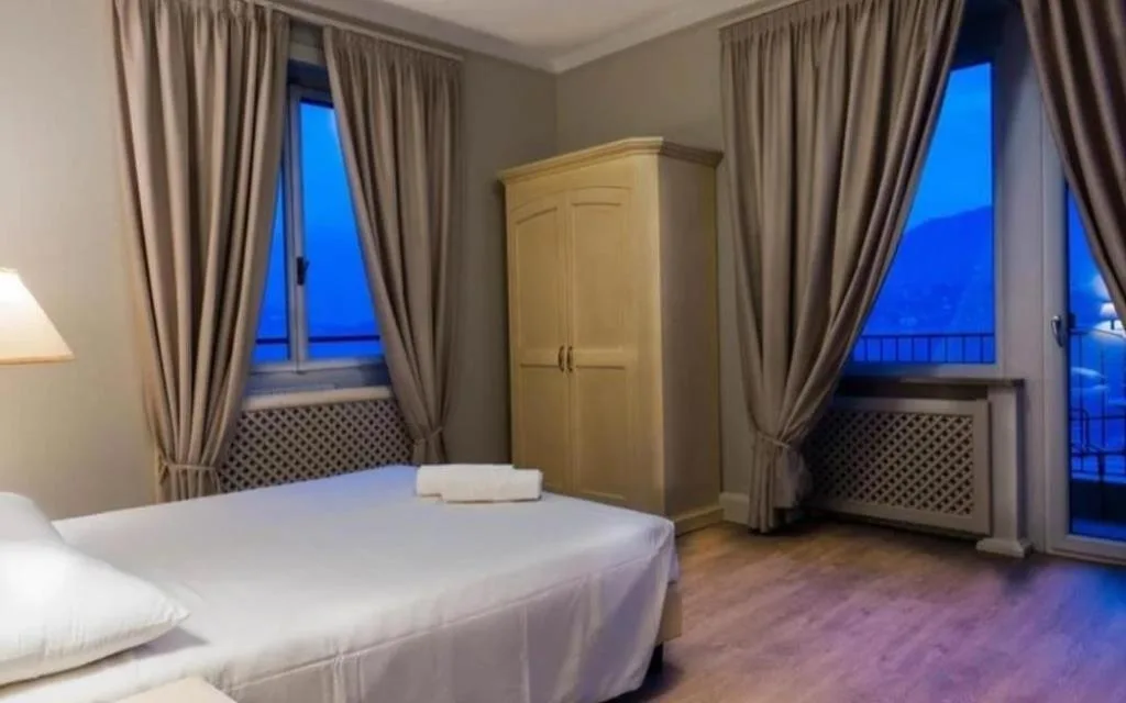 Camera con letto, armadio in legno e due finestre con vista serale sul lago