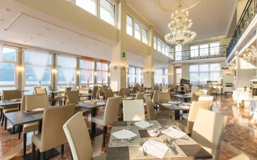 Sala ristorante elegante con lampadario in vetro, tavoli apparecchiati e vista lago