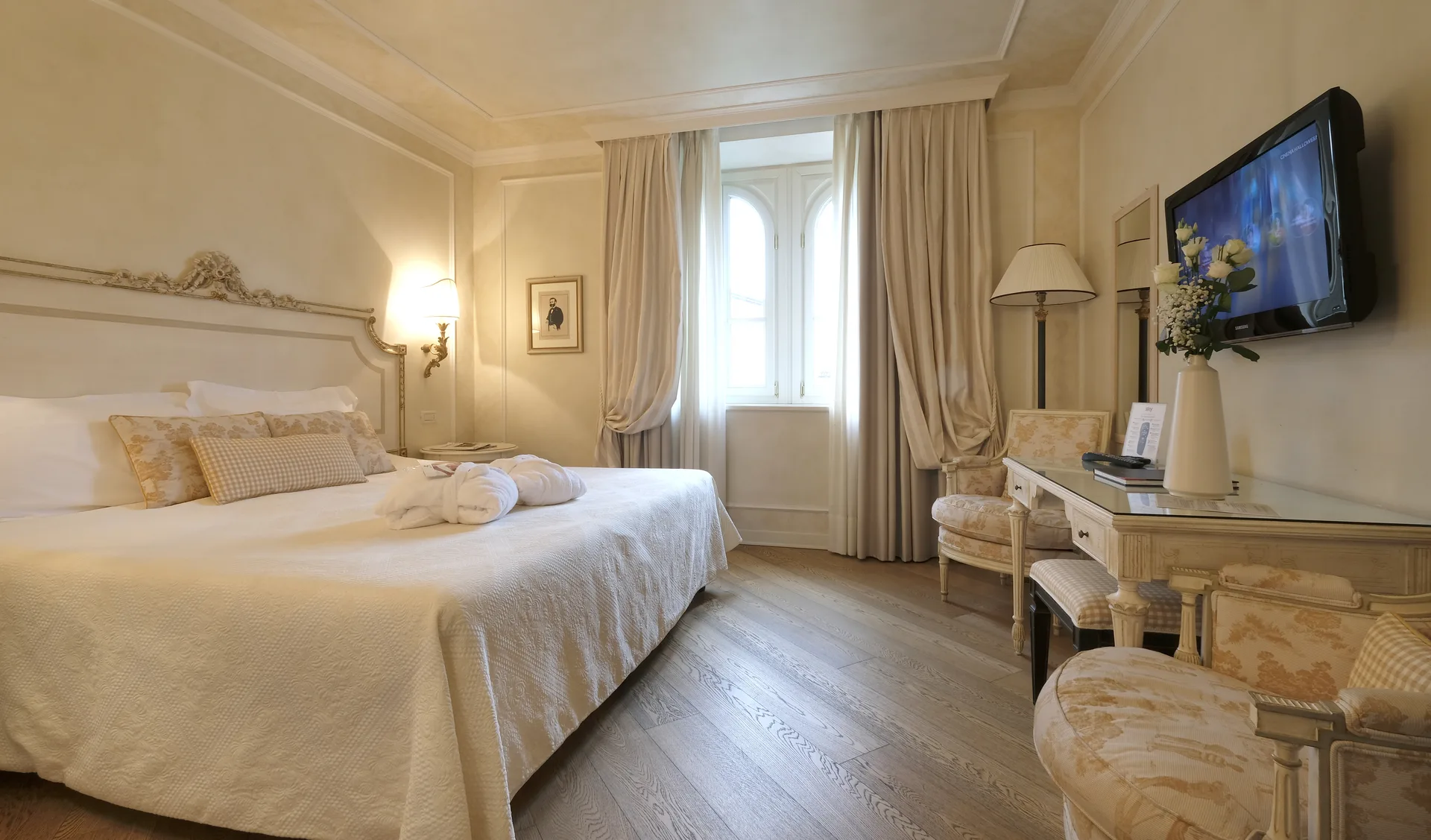 Camera classica in stile elegante con letto matrimoniale, tende beige, scrivania e TV