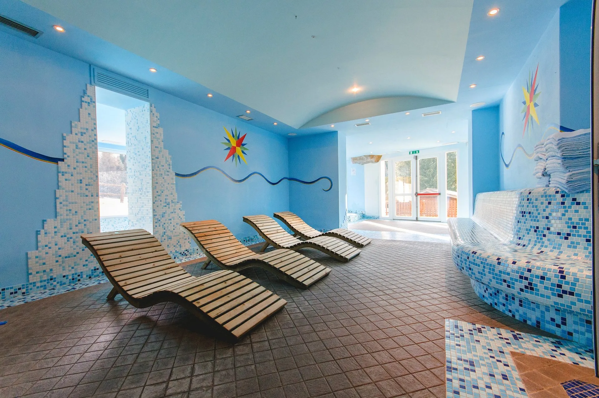 Area relax della spa con lettini in legno e pareti decorate con mosaico azzurro