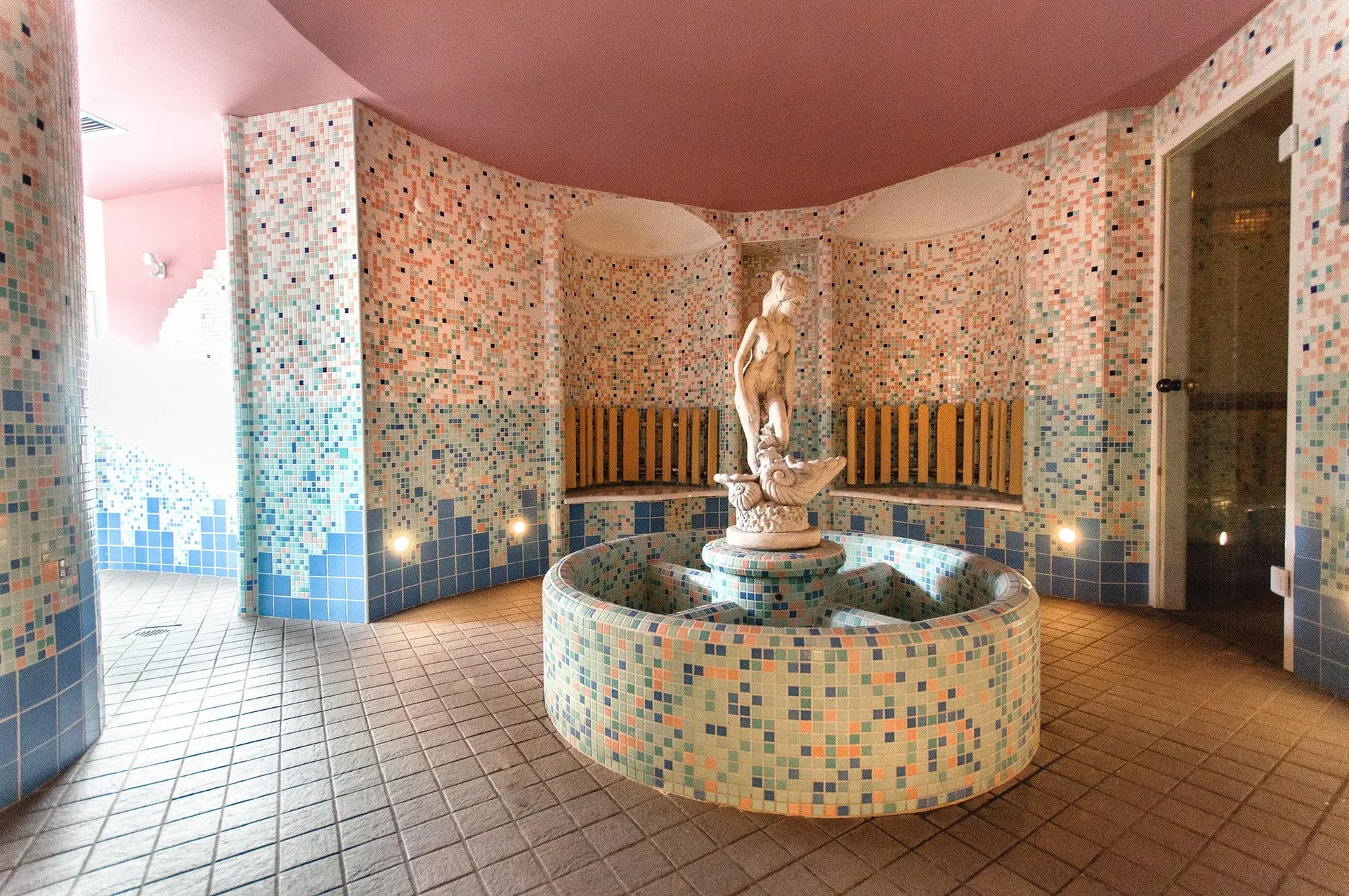 Sala benessere con vasca centrale mosaicata, statua in pietra e ingresso alla sauna