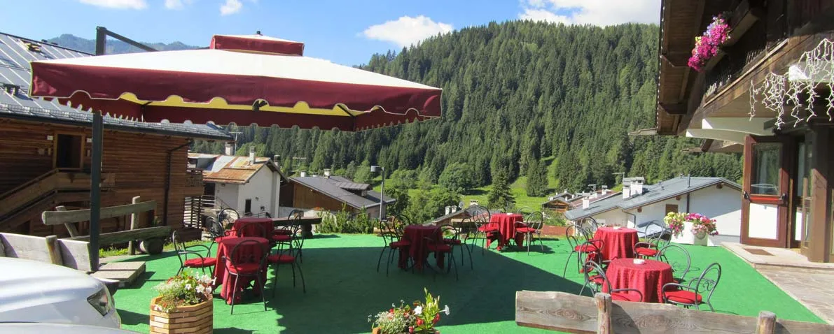 Terrazza esterna con tavolini rossi, ombrellone e vista sui boschi e sulle montagne