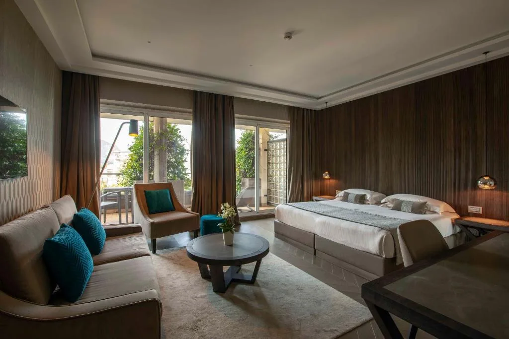 Suite elegante con letto, salotto, cuscini colorati e accesso al balcone