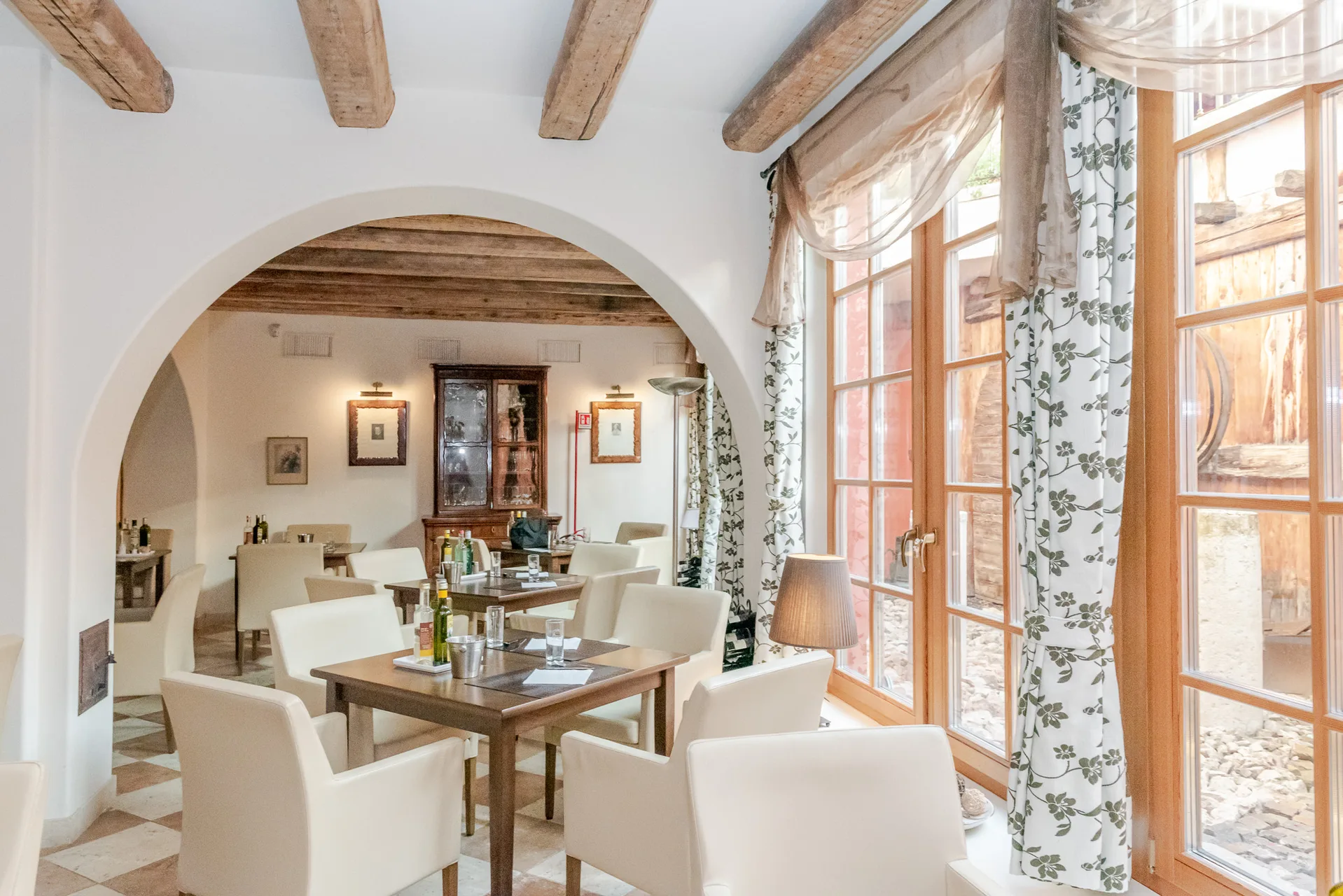 Sala ristorante con arco in muratura, tavoli apparecchiati e ampie finestre con tende floreali