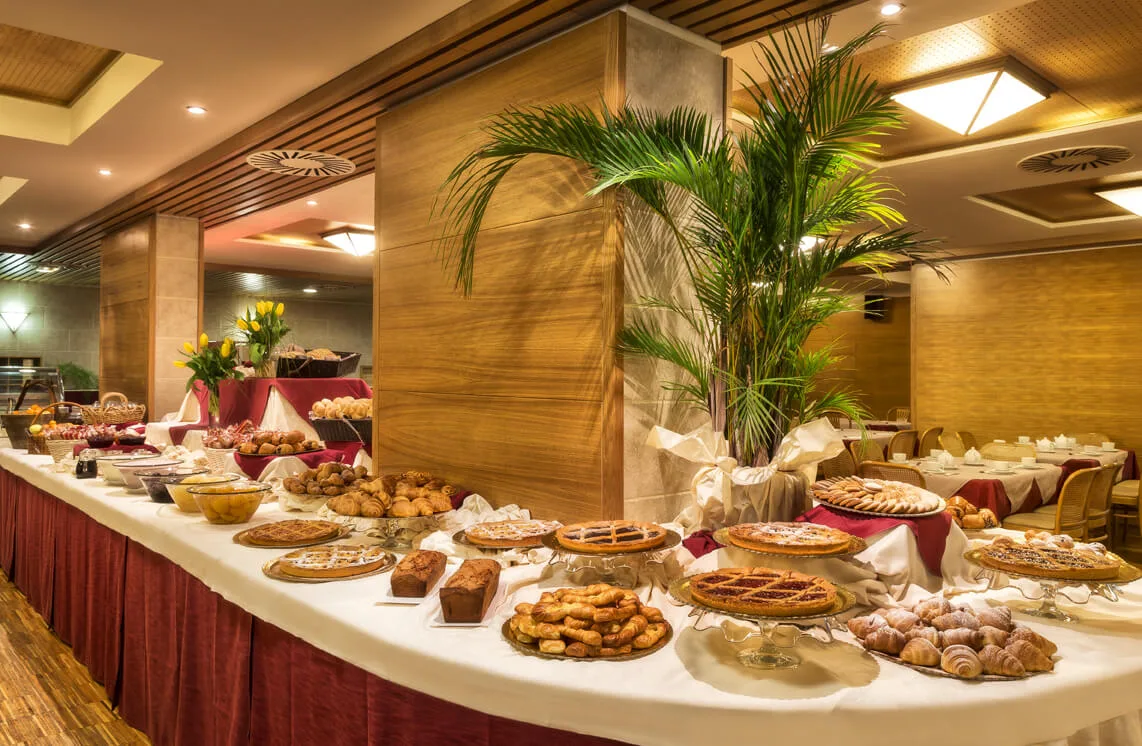 Buffet della colazione con dolci, crostate, cornetti e pane su lunga tavola decorata