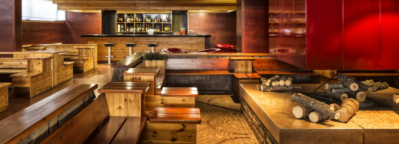 Bar interno con bancone in legno, panche rustiche e caminetto con legna