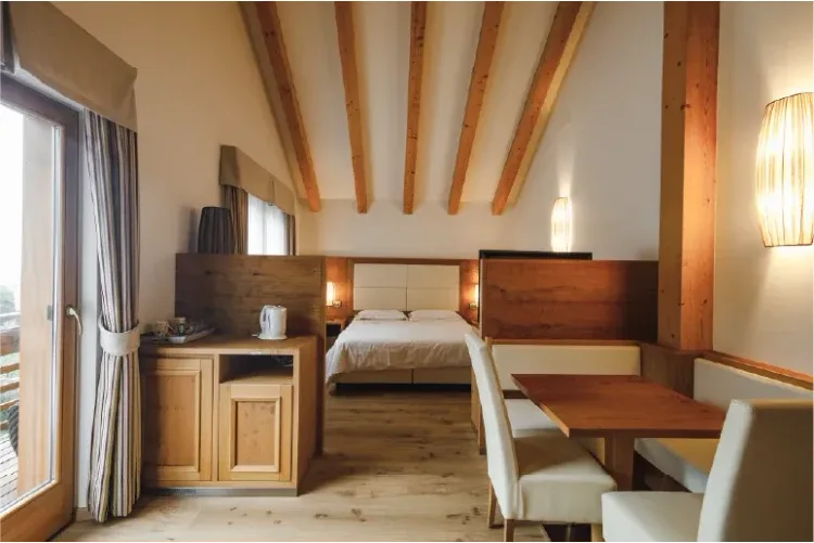 Camera mansardata con letto matrimoniale, travi a vista e angolo pranzo in legno