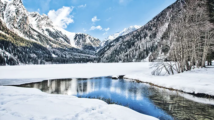 Lago alpino ghiacciato circondato da montagne e boschi innevati