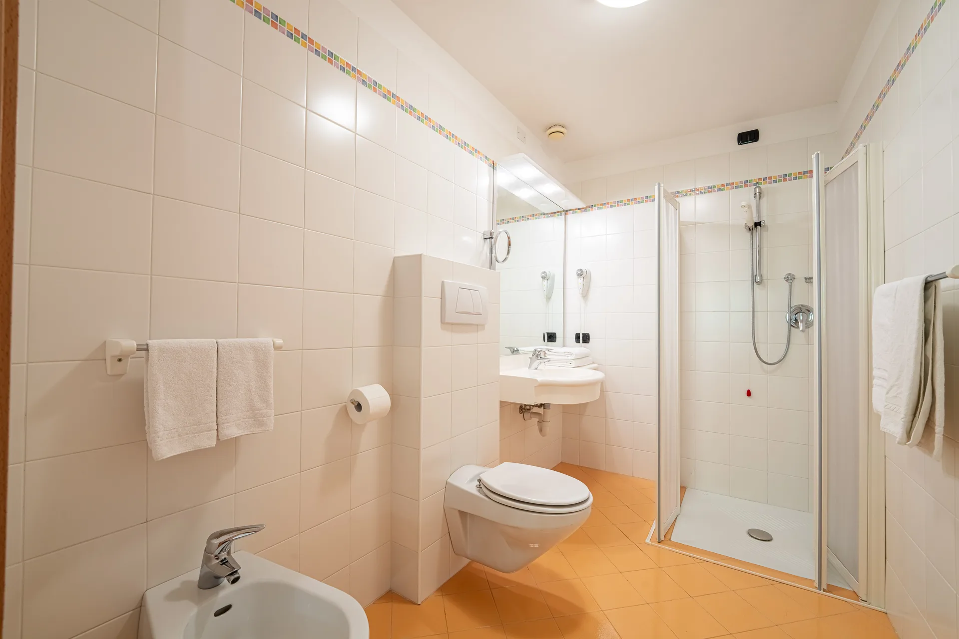 Bagno moderno piastrellato di bianco con doccia, WC, bidet, lavabo e specchio