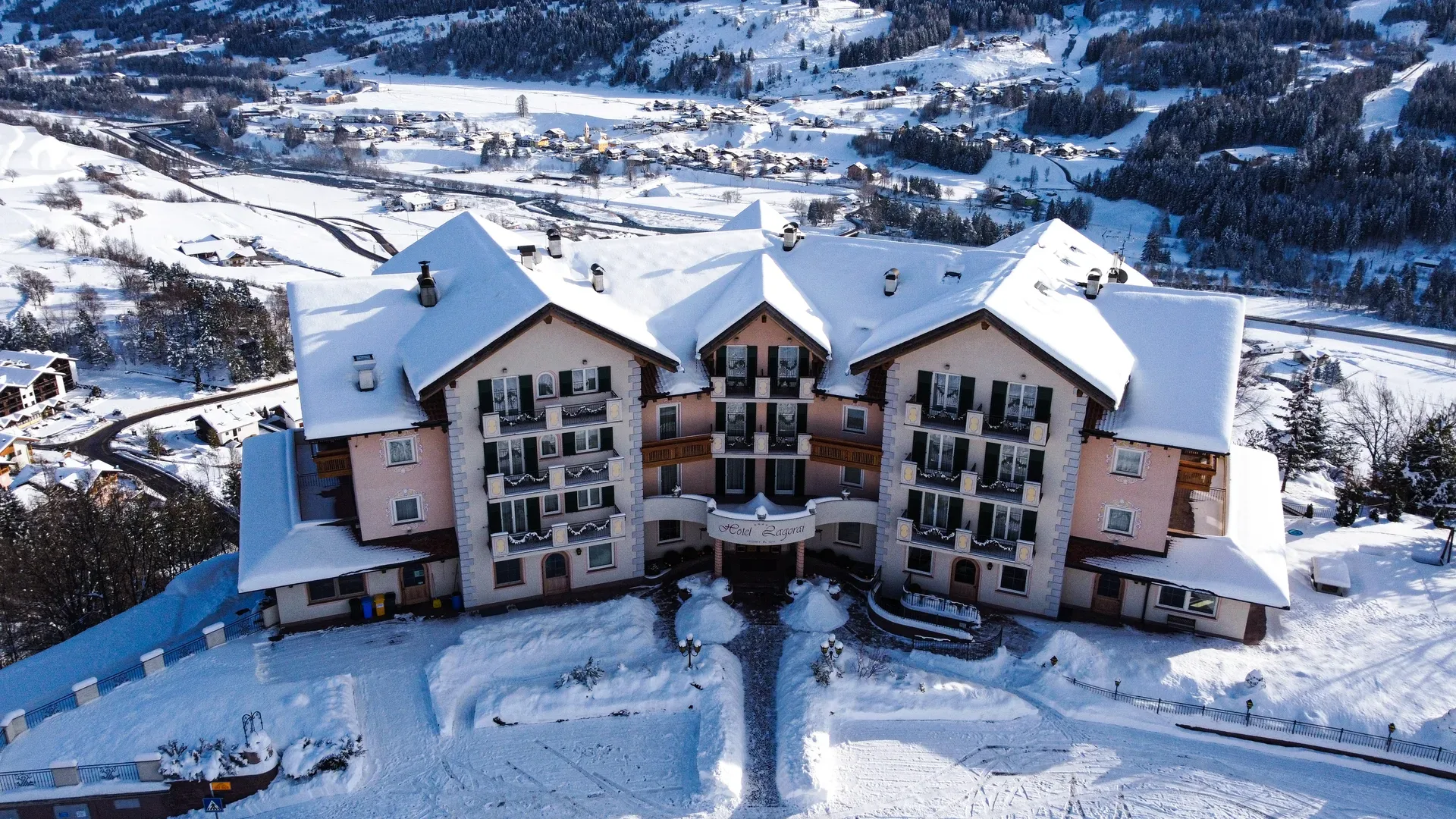Veduta aerea dell'Hotel Lagorai innevato con il paese e le montagne sullo sfondo