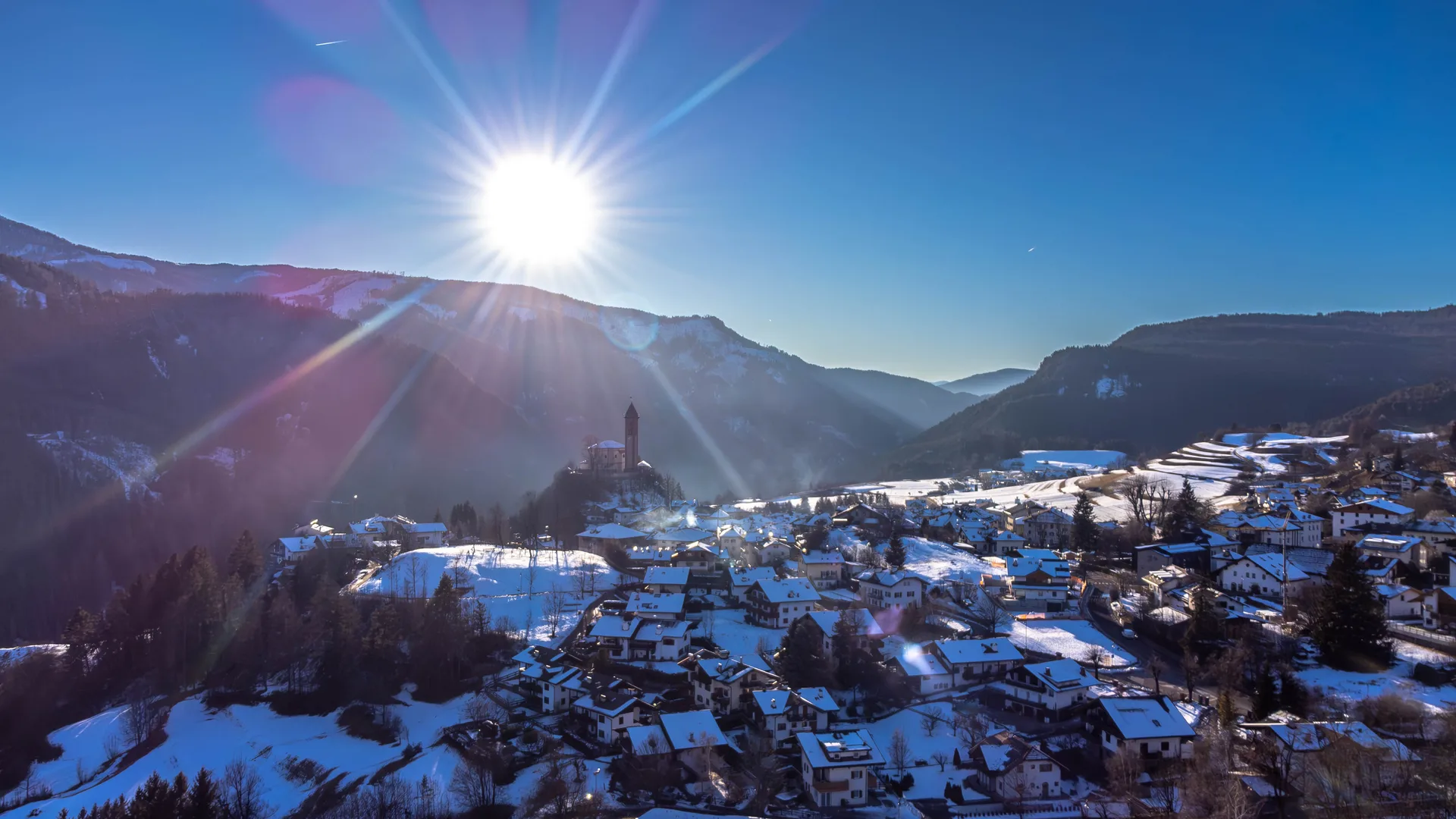 Vista aerea di paese di montagna innevato con sole e vette circostanti
