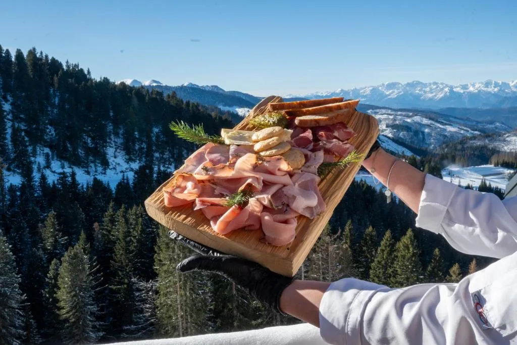 Tagliere di salumi e pane con panorama sulle montagne innevate