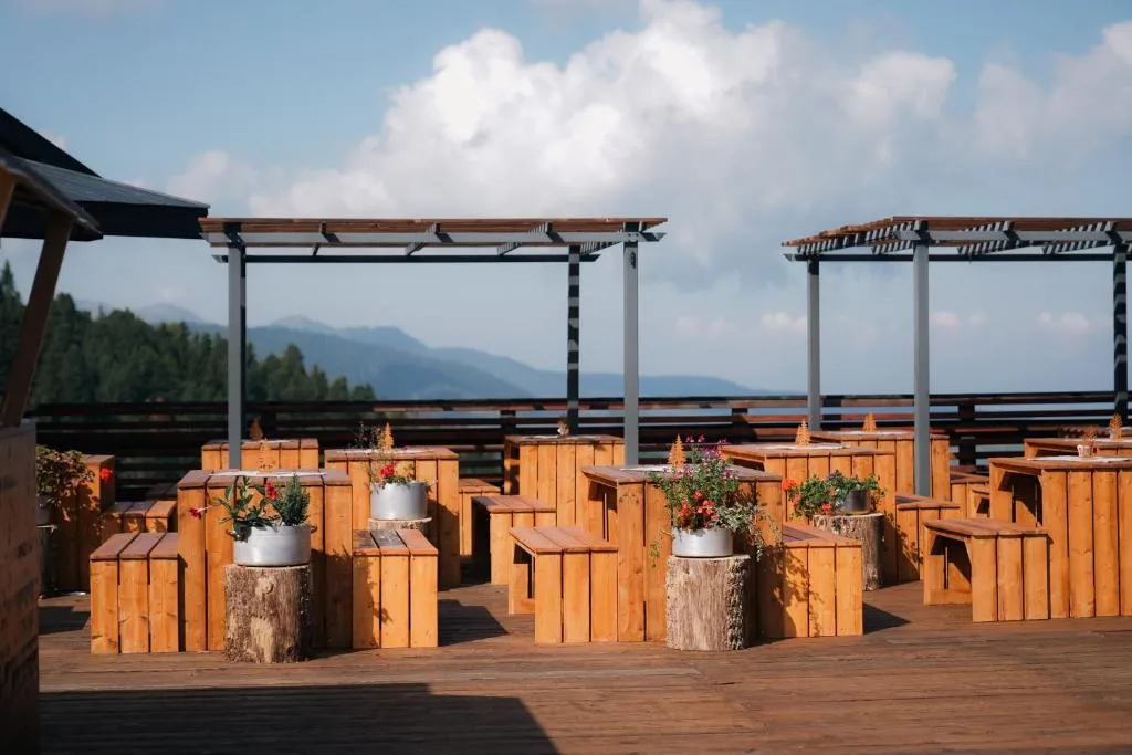 Terrazza panoramica in legno con tavoli, fiori e vista sulle montagne
