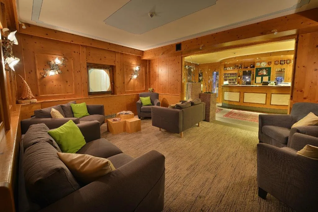 Hall dell'hotel con divani grigi, cuscini verdi e pareti in legno chiaro