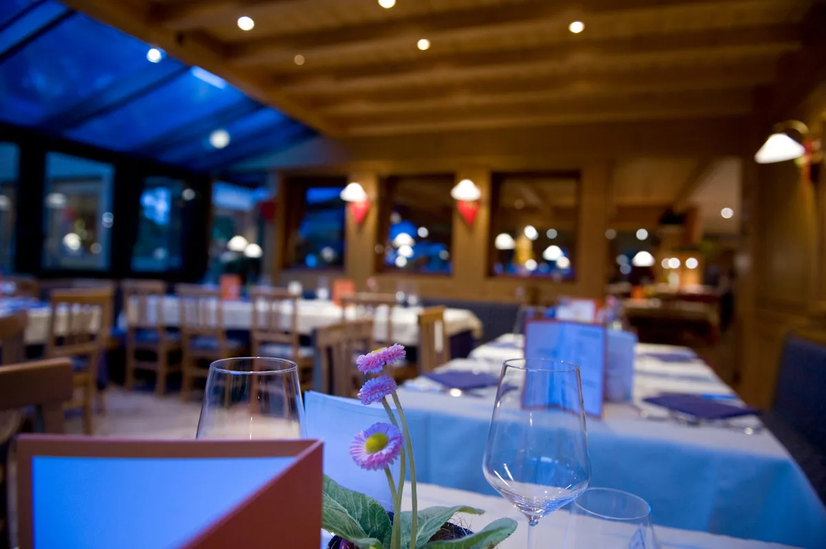 Tavoli del ristorante apparecchiati con calici e fiori in atmosfera serale