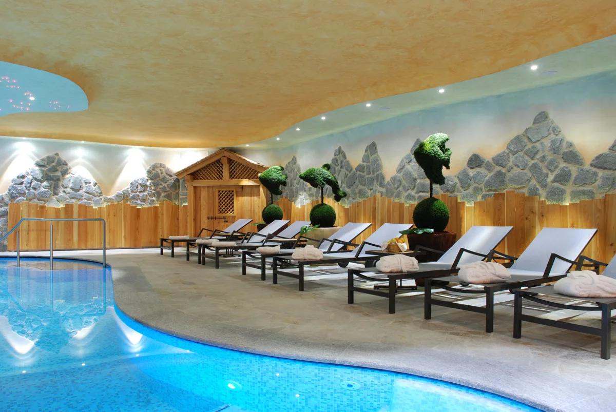 Zona relax bordo piscina con lettini bianchi e decorazioni topiaria