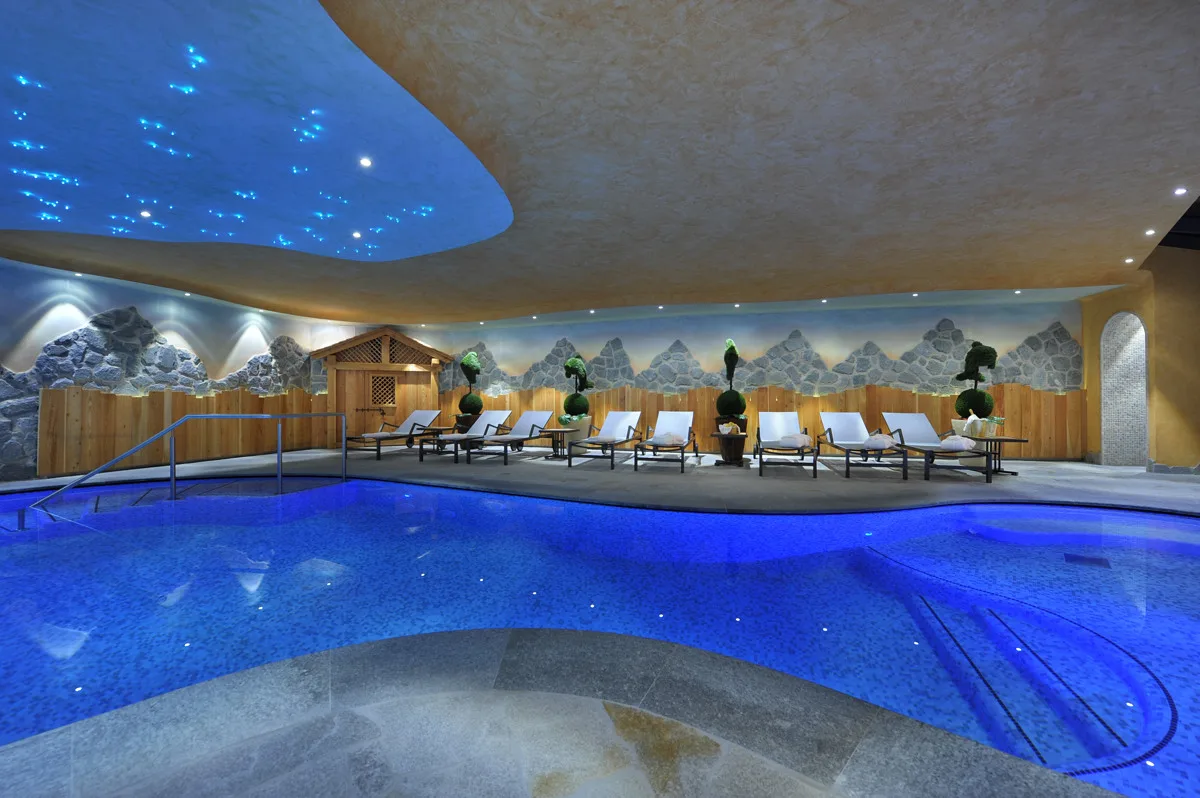 Piscina interna con lettini, decorazioni a tema montagna e soffitto luminoso blu